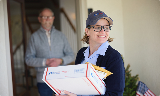Smiling postal employee holding packages at a customer's front door.